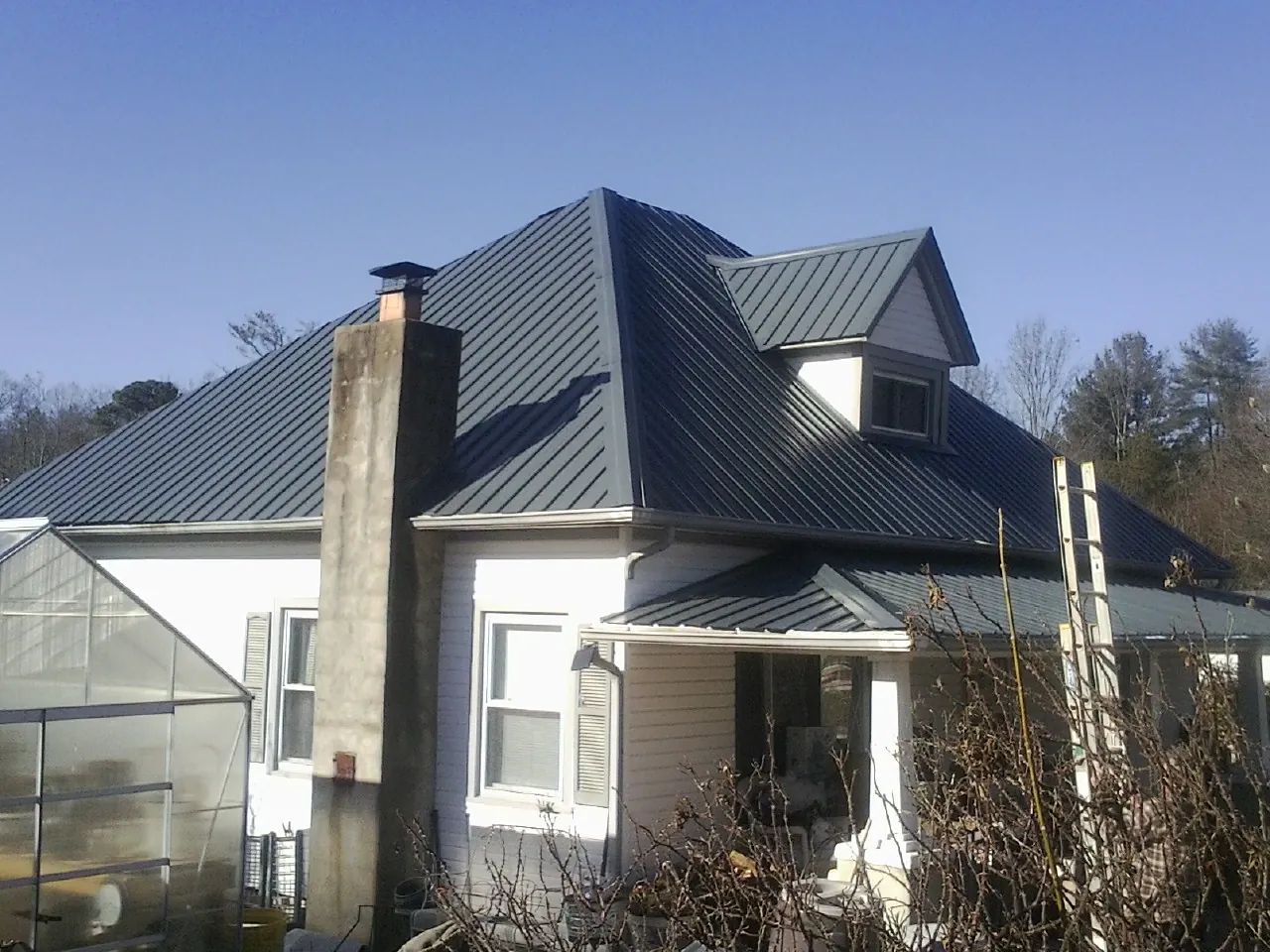 Dark blue standing seam metal roof on a white farmhouse with dormer in Pleasant Hill